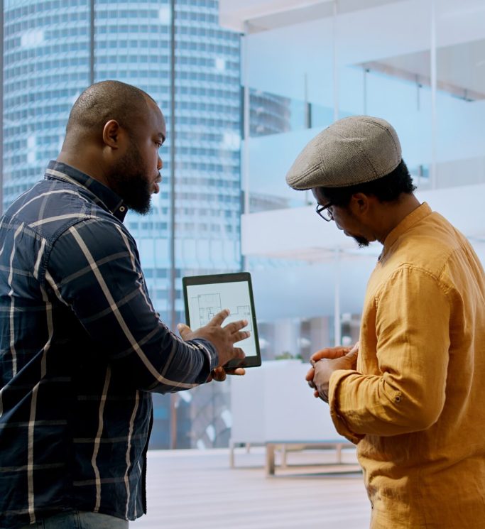 Real estate broker and client negotiating a leasing contract for a high class modern office space, evaluating blueprints on tablet during office tour. Property investment opportunity. Camera A.